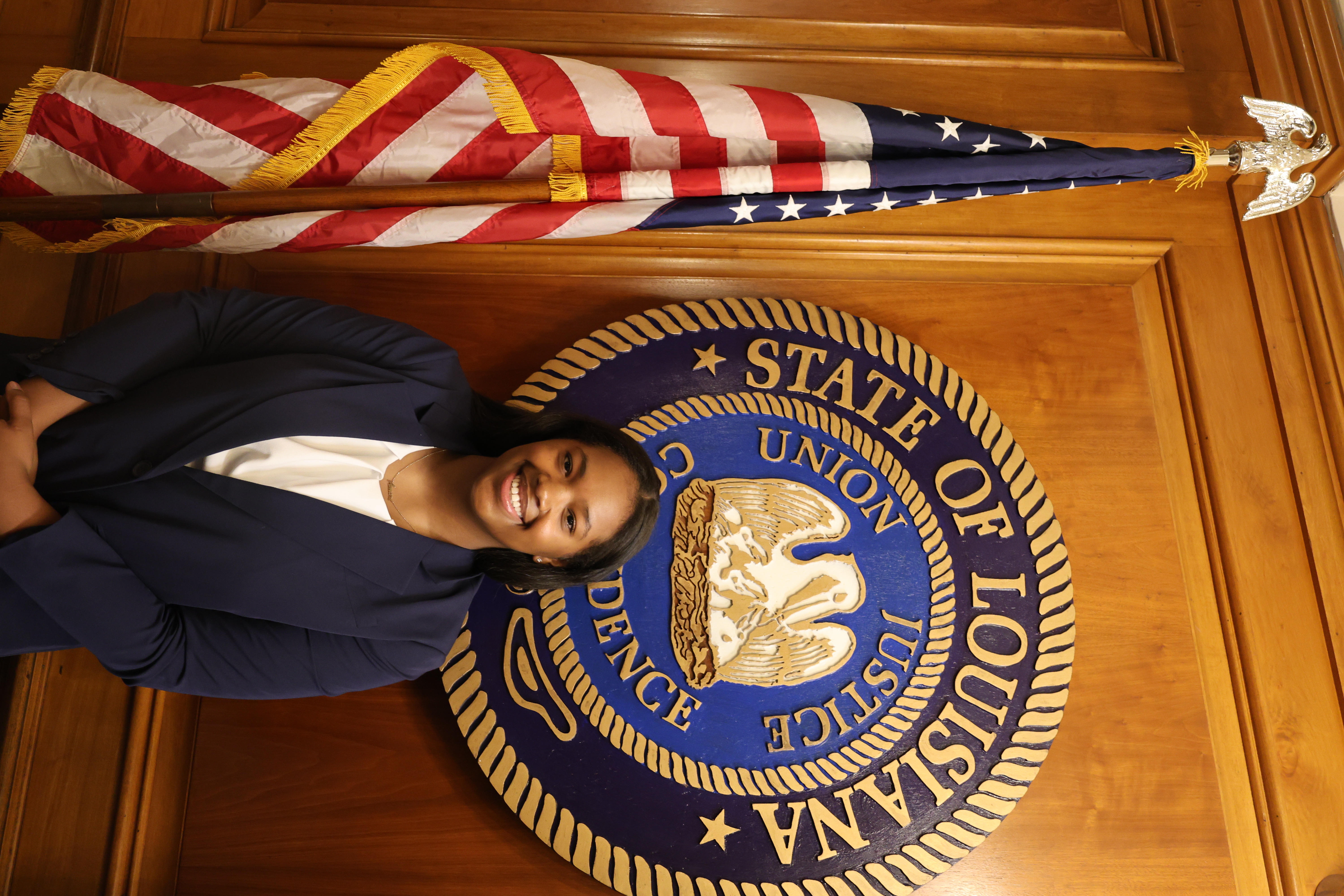 Headshot of girl in front of the Louisiana State symbol and American Flag