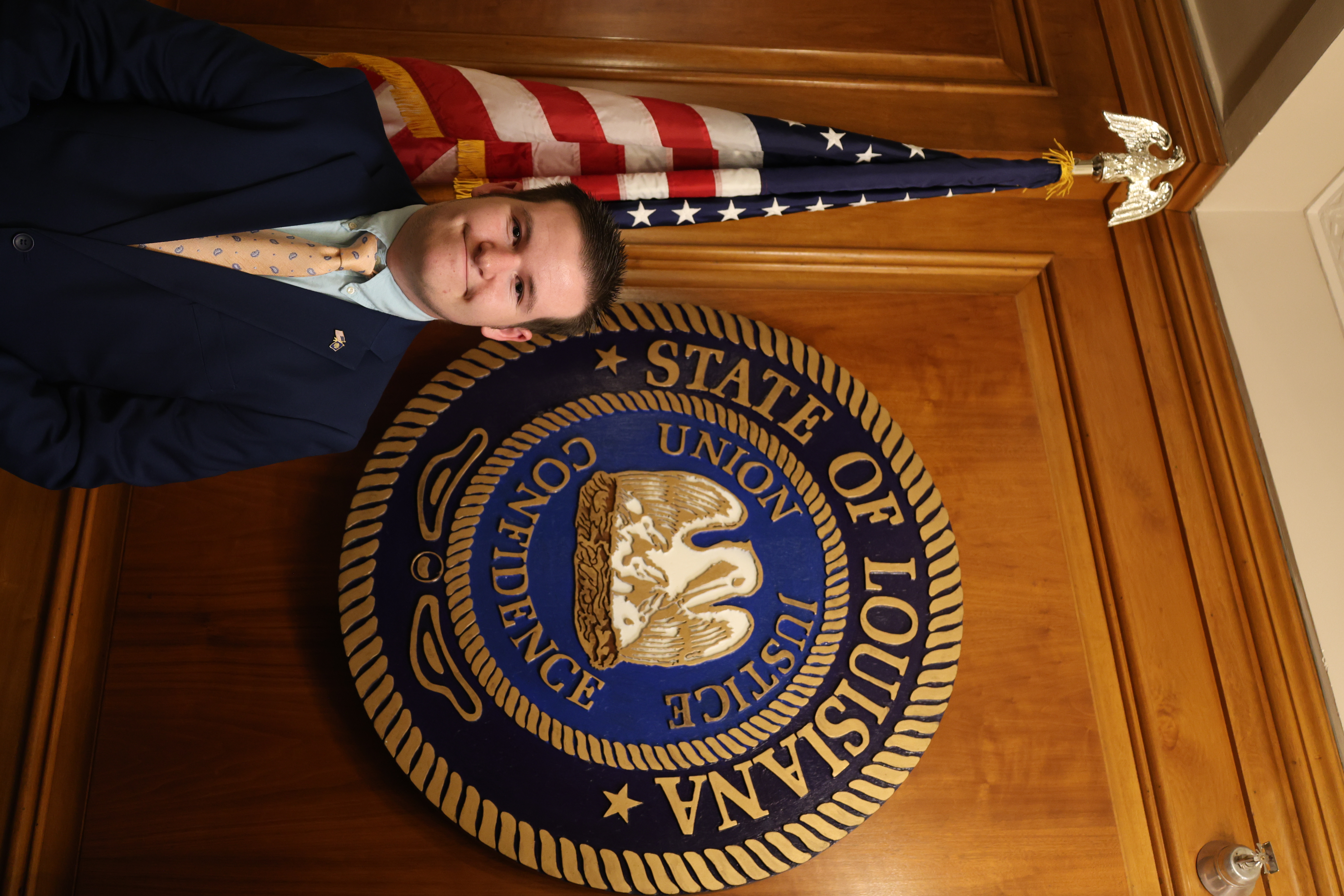 Headshot of boy in front of the Louisiana State symbol and American Flag