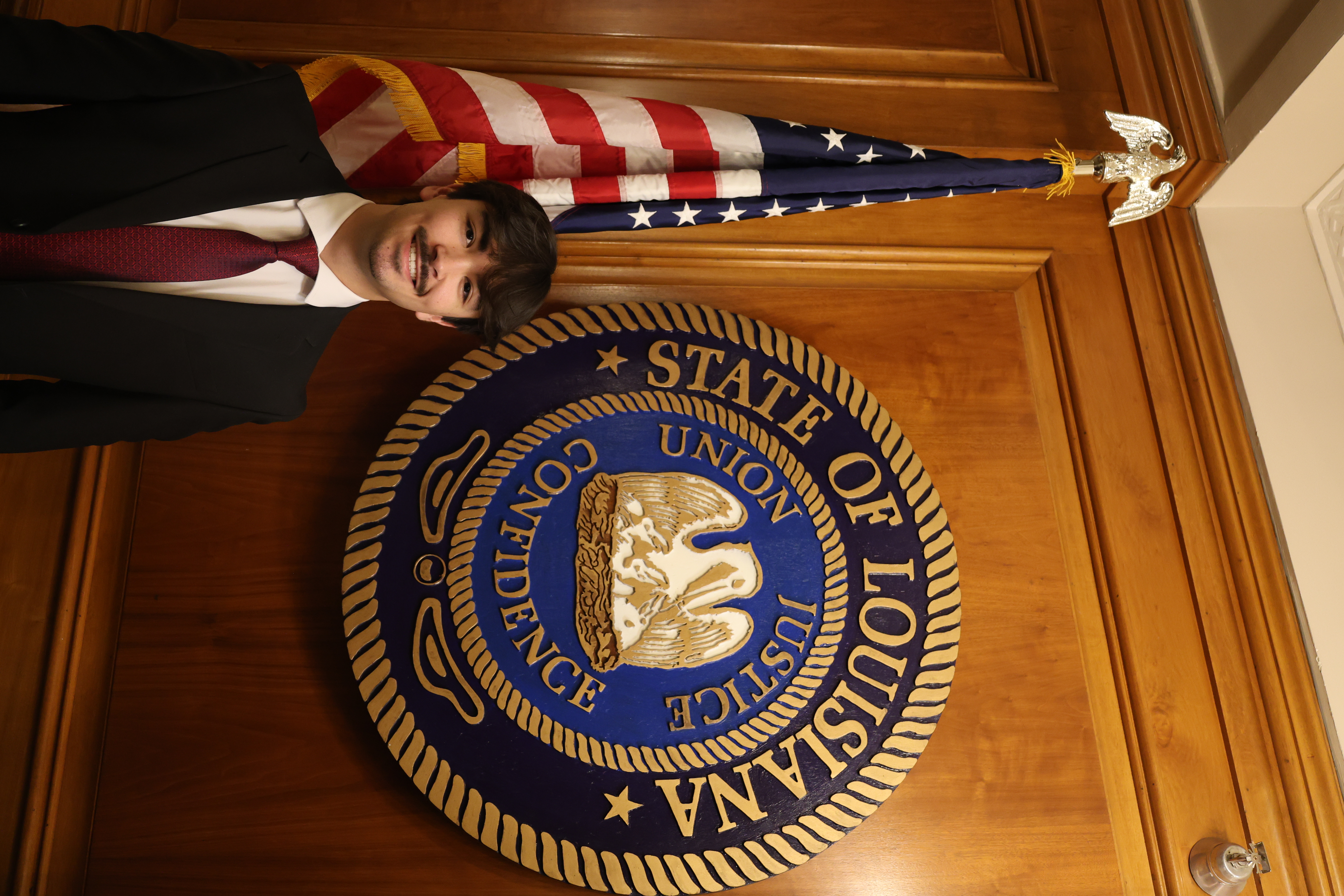 Headshot of boy in front of the Louisiana State symbol and American Flag