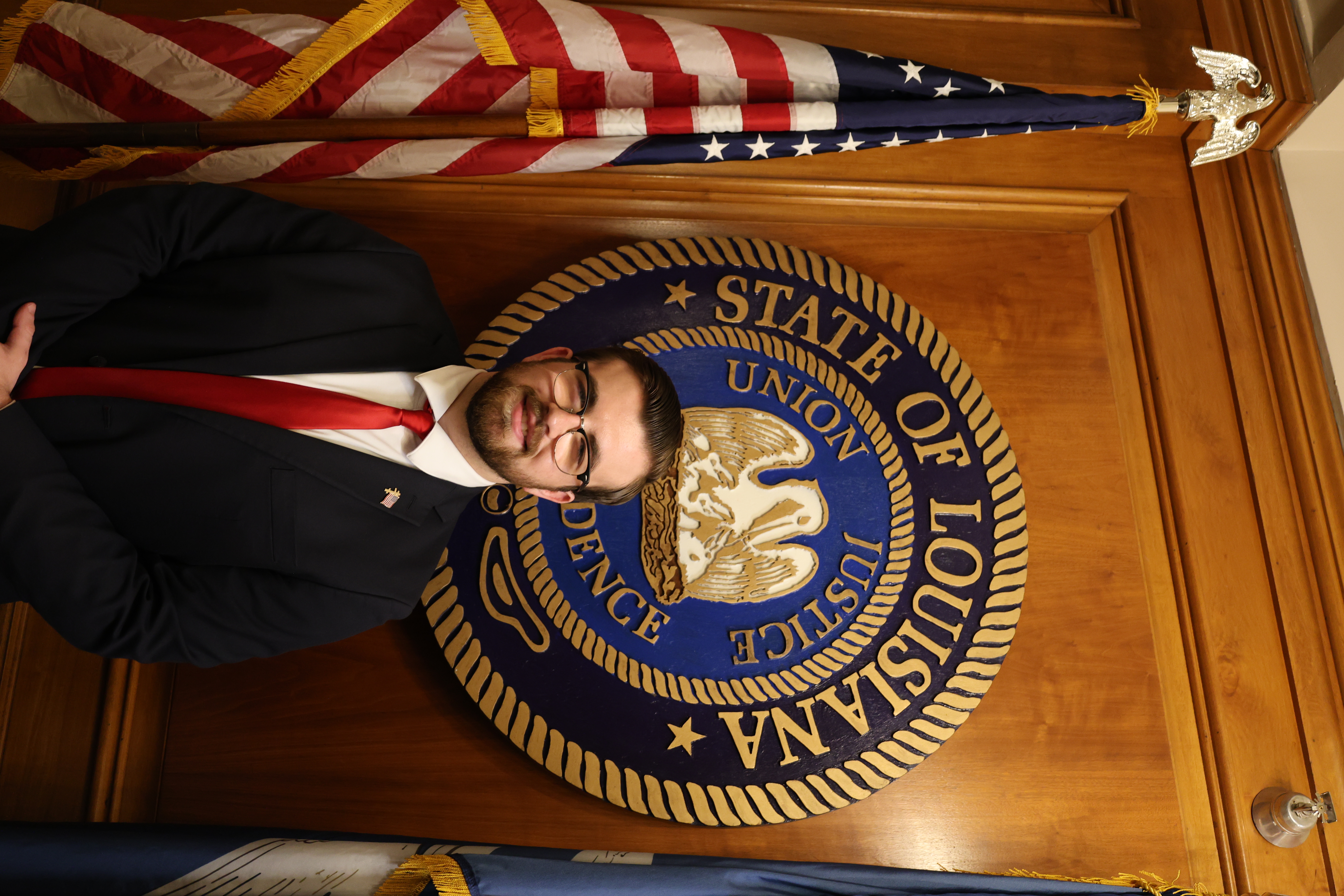 Headshot of boy in front of the Louisiana State symbol and American Flag